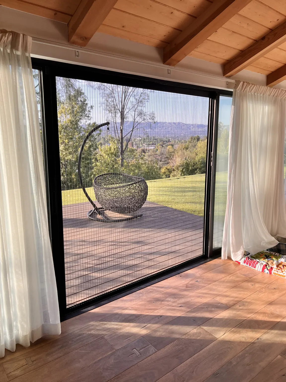 Aire pleated screen drawn across a slider with a hillside valley view beyond